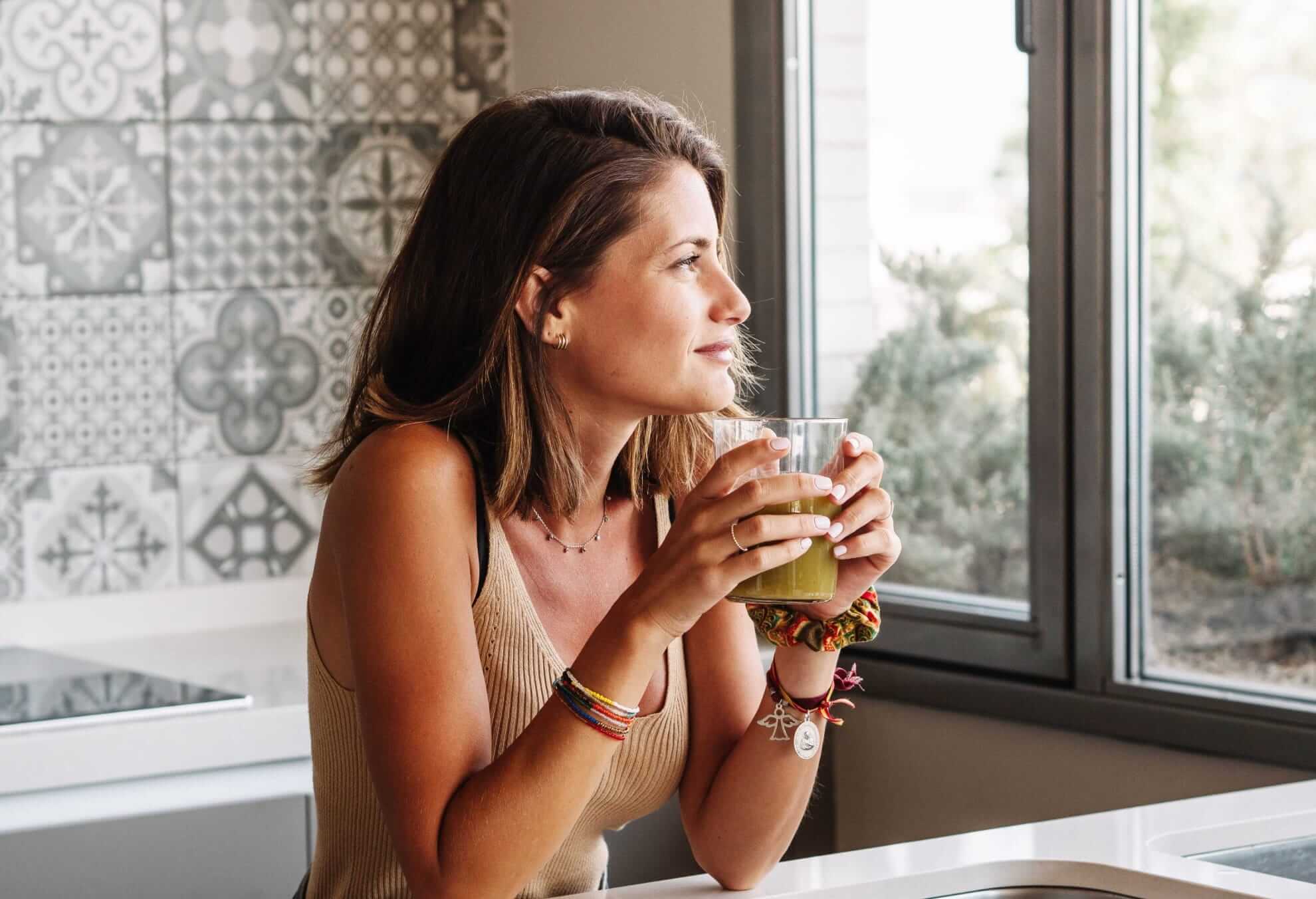 a woman holding a glass of tea in hand and looking at the view