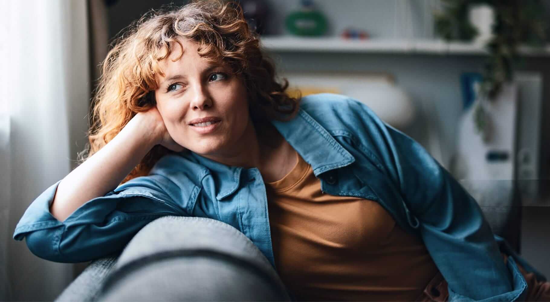 lounging on a grey couch, wearing a casual denim jacket
