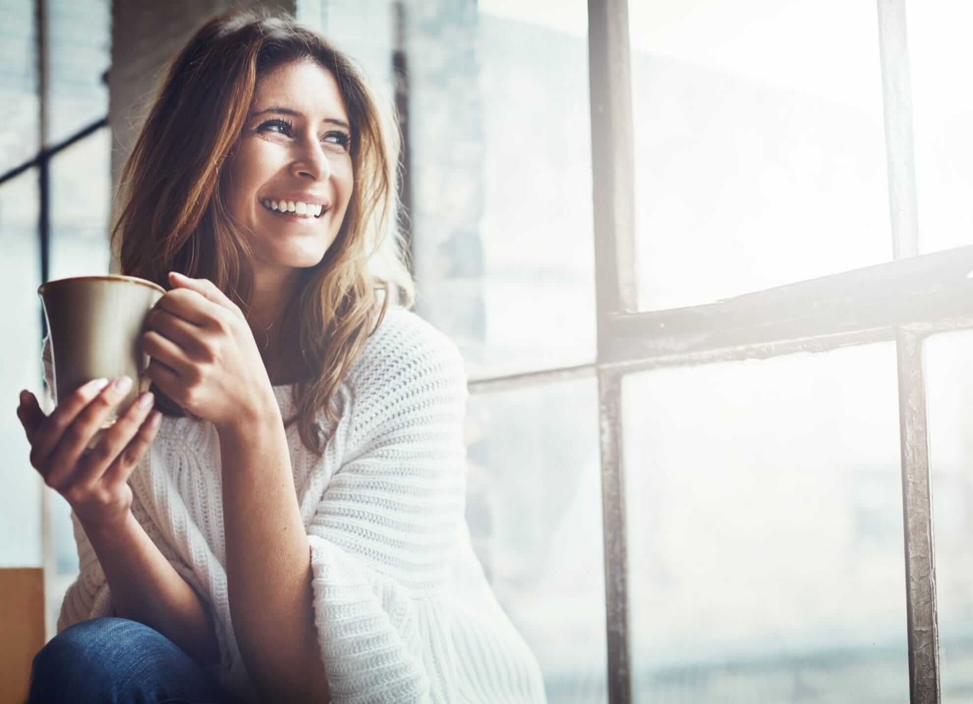 a woman enjoying a warm beverage in a ceramic mug, near a window