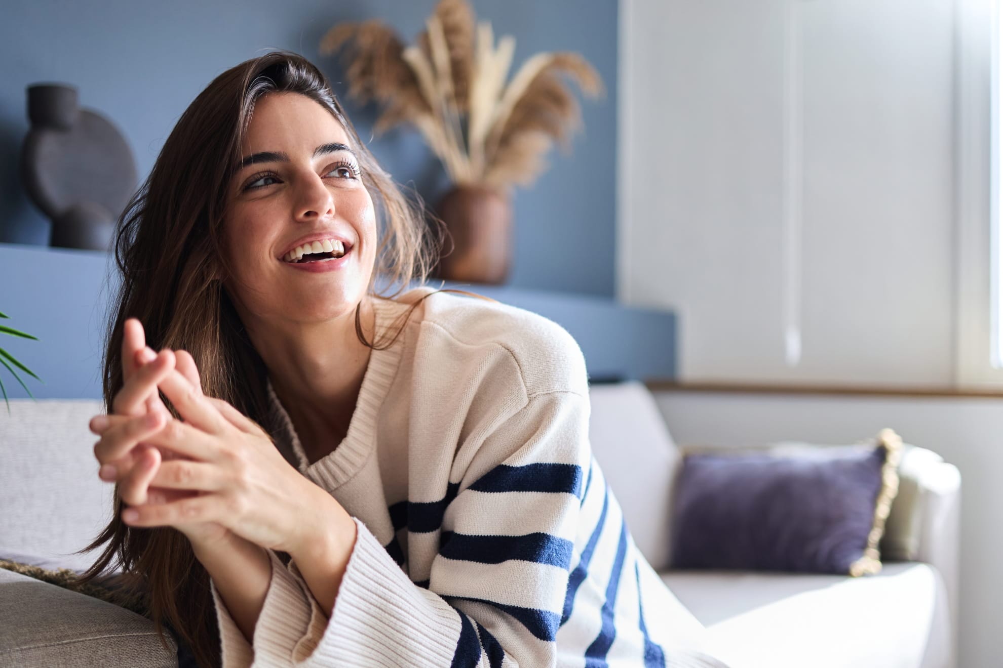 a woman smiling brightly while lounging in a cozy striped sweater on a comfortable sofa