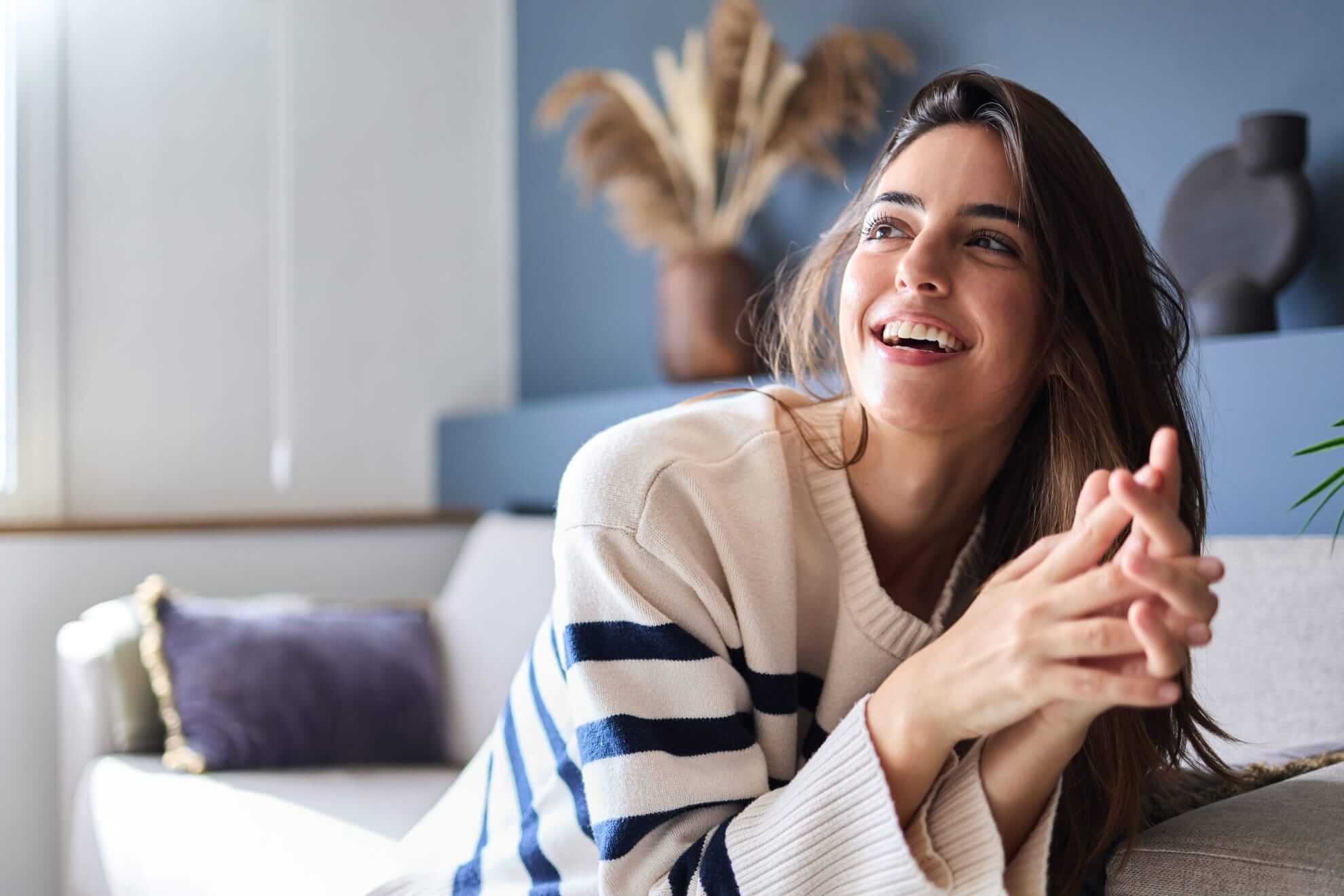 a woman smiling brightly while lounging in a cozy striped sweater on a comfortable sofa