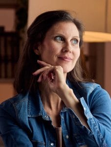A medium shot of a woman with brown hair and blue eyes, smiling thoughtfully