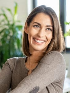 a woman smiling while wearing a comfortable brown sweater