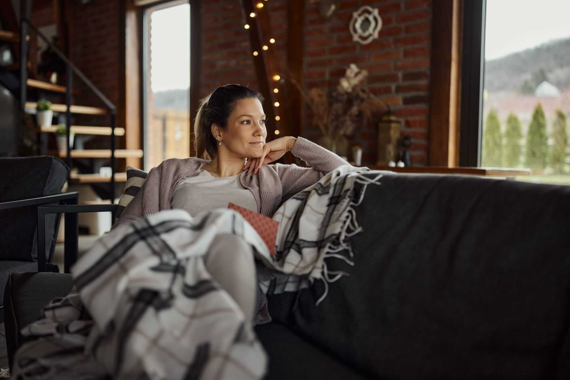 a woman lounging on a grey couch, draped in a white and black plaid blanket.